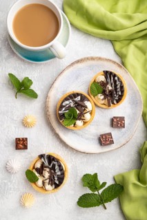 Sweet tartlets with chocolate and cheese cream with cup of coffee on a gray concrete background and