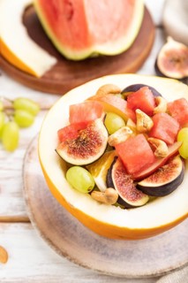 Vegetarian fruit salad of watermelon, grapes, figs, pear, orange, cashew on white wooden background