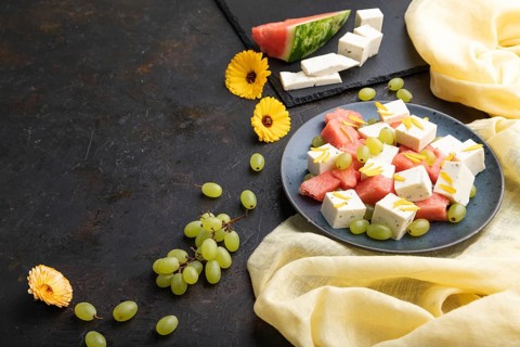 Vegetarian salad with watermelon, feta cheese, and grapes on blue ceramic plate on black concrete