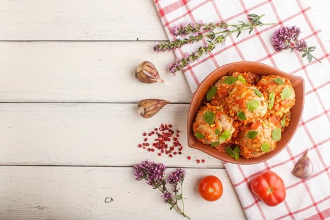 Pork meatballs with tomato sauce, oregano leaves, spices and herbs in clay bowl on a white wooden