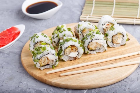 Japanese maki sushi rolls with green onion, chopsticks, soy sauce and marinated ginger on wooden