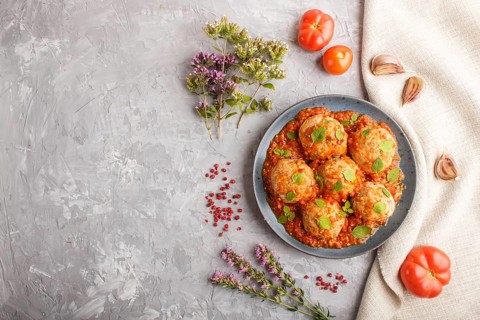 Pork meatballs with tomato sauce, oregano leaves, spices and herbs on blue ceramic plate on a gray