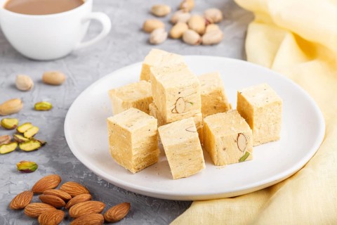 Traditional indian candy soan papdi in white plate with almond, pistache and a cup of coffee on a
