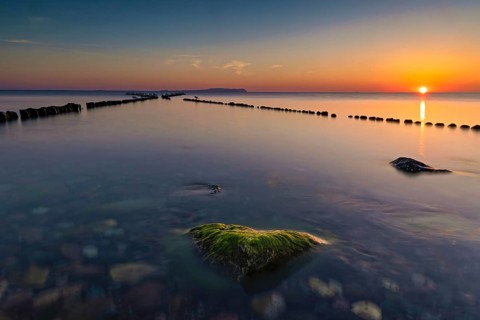 Sunset at the double stage in Dranske on the island of Ruegen. A green stone overgrown with algae