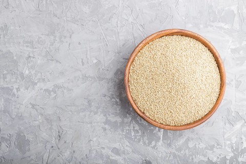 Wooden bowl with raw white quinoa seeds on a gray concrete background. Top view, flat lay, copy