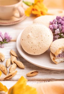 Meringues cakes with cup of coffee on a white wooden background and orange linen textile. Side