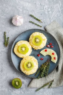 Pieces of baked pork with pineapple, cheese and kiwi on gray background, top view