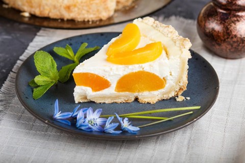 A piece of peach cheesecake on a blue ceramic plate with blue flowers and a cup of coffee on a