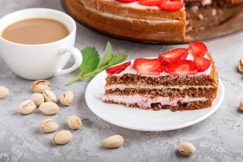 Homemade cake with yoghurt cream, strawberry, pistachio and a cup of coffee on a gray concrete