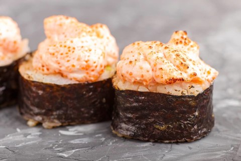 Japanese maki sushi rolls with flying fish roe, cheese on black concrete background. Side view,