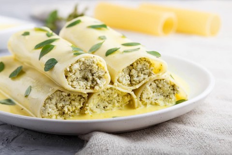 Cannelloni pasta with egg sauce, cream cheese and oregano leaves on a gray concrete background with