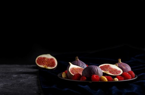Fresh figs, strawberries and raspberries on blue ceramic plate on black concrete background and