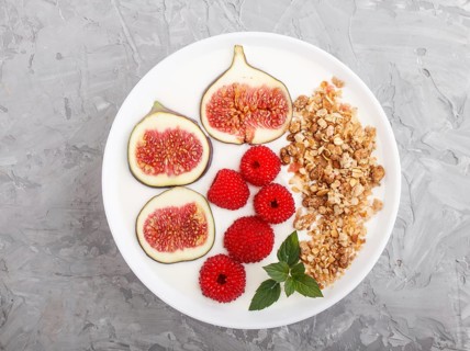 Yoghurt with raspberry, granola and figs in white plate on a gray concrete background top view,