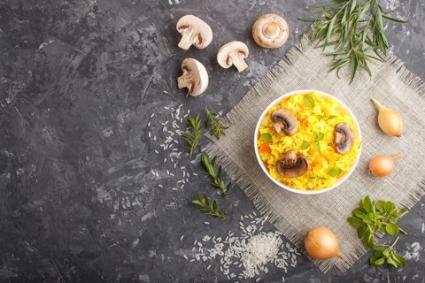 Yellow fried rice with champignons mushrooms, turmeric and oregano in white ceramic bowl on a black