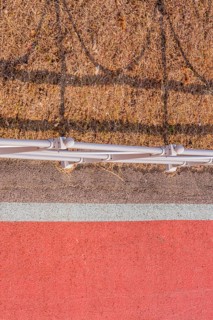 Looking down onto red bike path next to metal guardrail casting its shadow on brown grassy area in