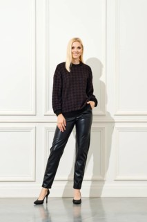 An elegant woman poses confidently against a white, panelled wall. She is dressed in a dark,
