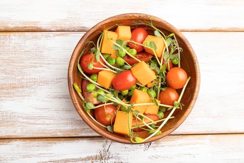 Vegetarian vegetable salad of tomatoes, pumpkin, microgreen pea sprouts on white wooden background.