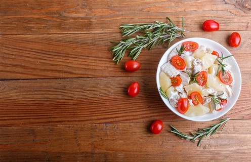Chicken fillet salad with rosemary, pineapple and cherry tomatoes on brown wooden background. top