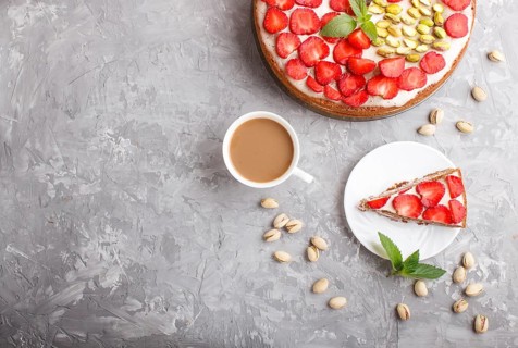 Homemade cake with yoghurt cream, strawberry, pistachio and a cup of coffee on a gray concrete