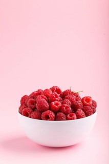 Fresh raspberry in white bowl on pink pastel background. side view, copy space