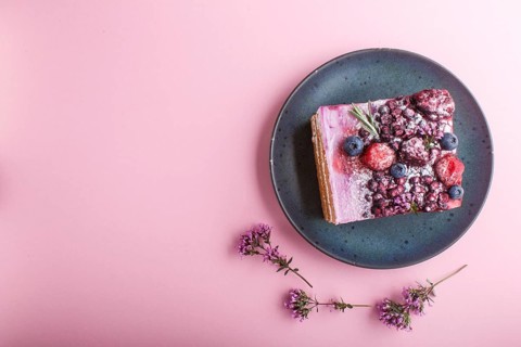 Berry cake with milk cream and blueberry jam on blue ceramic plate on a pink pastel background. top