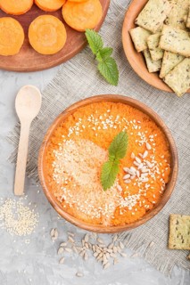 Carrot cream soup with sesame seeds and snacks in wooden bowl on a gray concrete background with