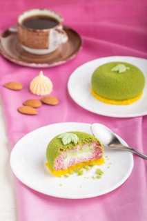 Green mousse cake with pistachio and strawberry cream on a white wooden background and pink textile