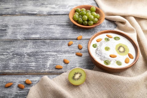 Yogurt with kiwi, gooseberry, chia and almonds in wooden bowl on gray wooden background and linen