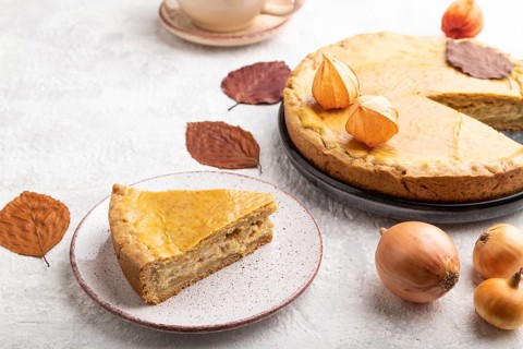 Autumn onion pie decorated with leaves and cup of coffee on gray concrete background. Side view,