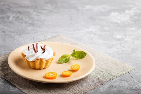 Cake with whipped egg cream on a light brown plate with kumquat slices and mint leaves on a gray