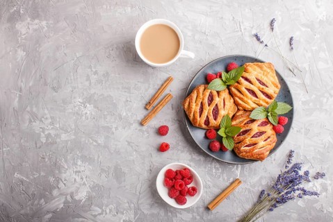 Puff pastry buns with strawberry jam on blue ceramic plate on gray concrete background, cup of