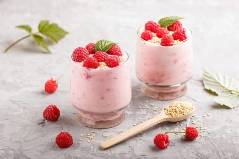 Yoghurt with raspberry and sesame in a glass and wooden spoon on gray concrete background. side