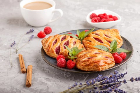 Puff pastry buns with strawberry jam on blue ceramic plate on gray concrete background, cup of