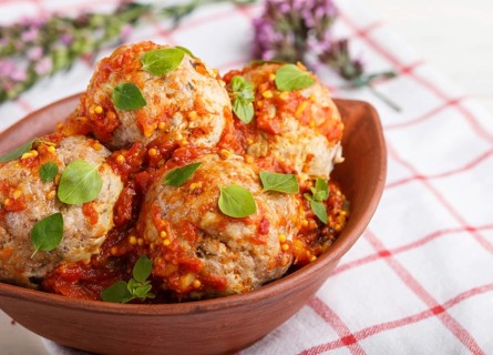 Pork meatballs with tomato sauce, oregano leaves, spices and herbs in clay bowl on a white wooden