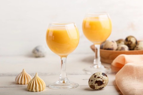Sweet egg liqueur in glass with quail eggs and meringues on white wooden background. Side view,
