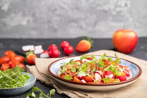Vegetarian fruits and vegetables salad of strawberry, kiwi, tomatoes, microgreen sprouts on black