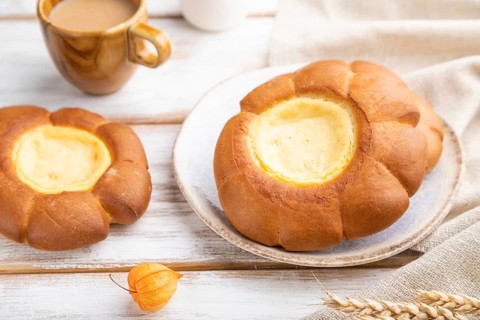 Sour cream bun with cup of coffee on a white wooden background and linen textile. Side view, close
