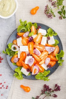 Vegetarian salad with fresh grape tomatoes, feta cheese, lettuce and onion on blue ceramic plate on