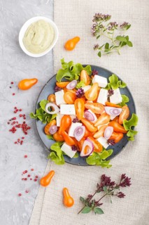 Vegetarian salad with fresh grape tomatoes, feta cheese, lettuce and onion on blue ceramic plate on