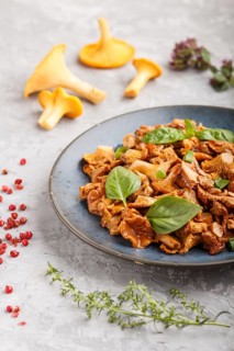 Fried chanterelle mushrooms with basil and spice herbs on gray concrete background. Side view,