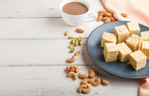 Traditional indian candy soan papdi in a blue ceramic plate with almond, pistache, cashew and a cup