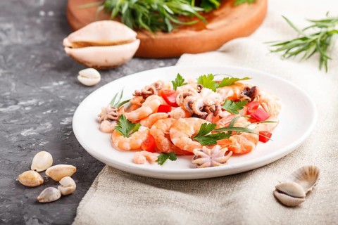 Boiled shrimps or prawns and small octopuses with herbs on white ceramic plate on a black concrete