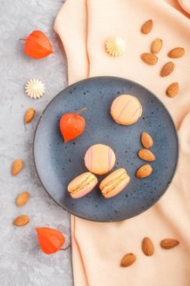 Orange macarons or macaroons cakes on blue ceramic plate on a gray concrete background and orange