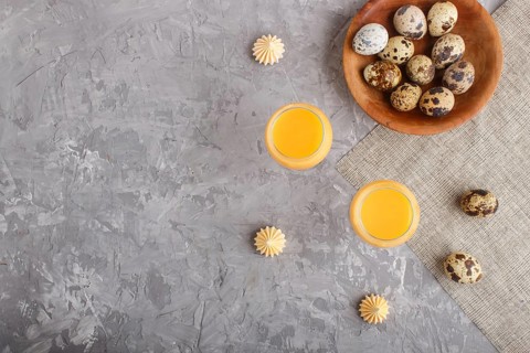 Sweet egg liqueur in glass with quail eggs and meringues on a gray concrete background. Top view,