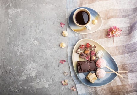 A pieces of homemade chocolate with coconut candies and a cup of coffee on a gray concrete