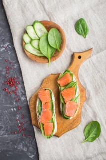Smoked salmon sandwiches with cucumber and spinach on wooden board on a black concrete background.