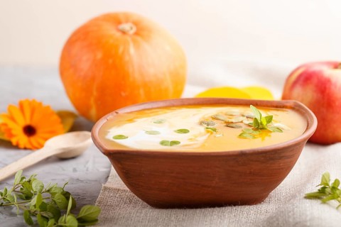 Traditional pumpkin cream soup with seeds in clay bowl on a gray concrete background with linen