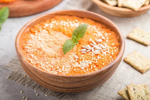 Carrot cream soup with sesame seeds and snacks in wooden bowl on a gray concrete background with