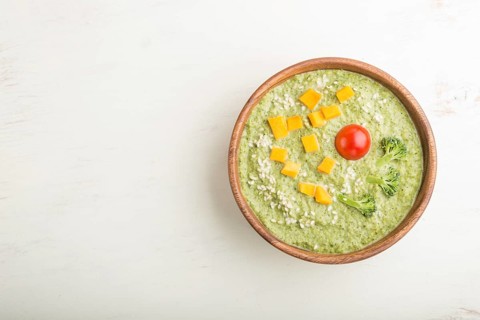 Green broccoli cream soup in wooden bowl on a white wooden background. top view, flat lay, copy