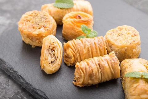 Traditional arabic sweets (kunafa, baklava) on a black slate board on a black concrete background.